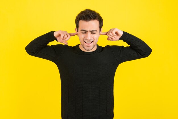 Retrato de hombre joven tapándose las orejas sobre la pared amarilla