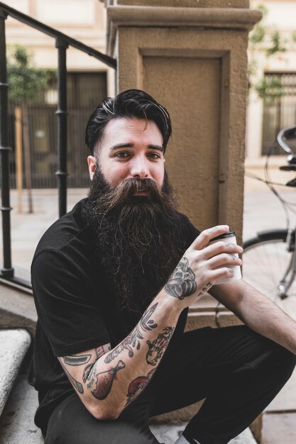 Retrato de hombre joven con tatuaje en su mano sosteniendo la taza de café