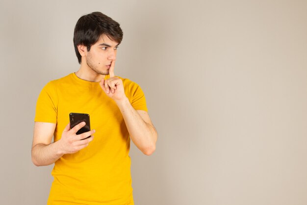 Retrato de un hombre joven con un teléfono móvil contra el gris.