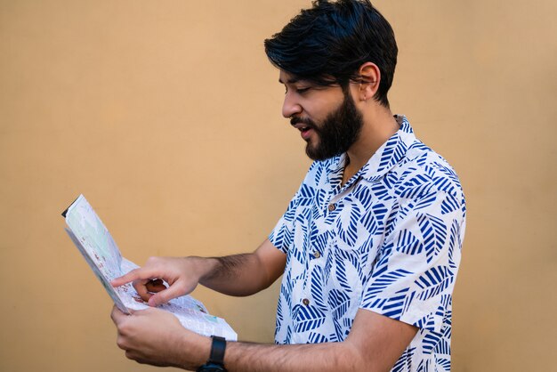 Retrato de hombre joven turista con ropa de verano y sosteniendo un mapa en busca de direcciones contra el amarillo.