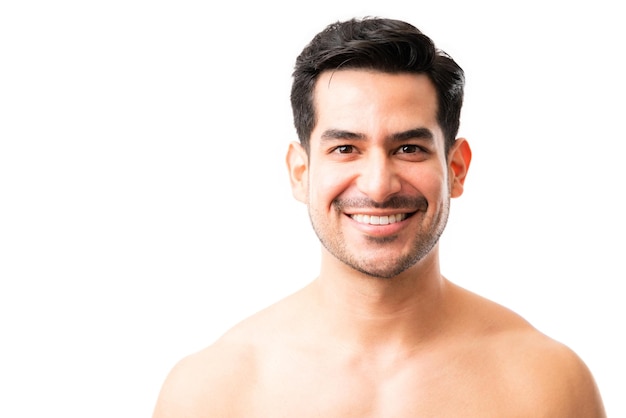 Retrato de un hombre latino de 20 años mirando a la cámara y sonriendo sobre fondo blanco.