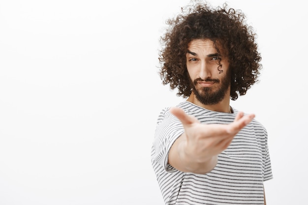 Retrato de hombre macho guapo confiado con barba y cabello rizado, tirando de la mano hacia