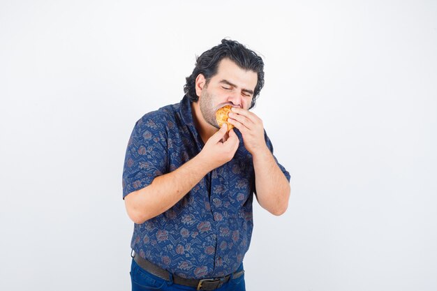 Retrato de hombre maduro comiendo productos de pastelería en camisa y mirando encantados vista frontal