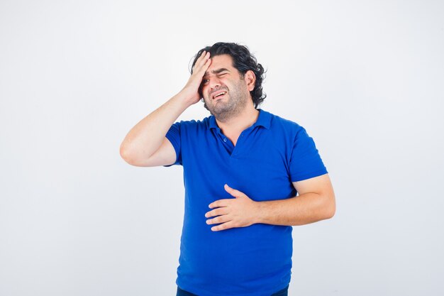 Retrato de hombre maduro que sufre de un fuerte dolor de cabeza en camiseta azul y mirando molesto vista frontal