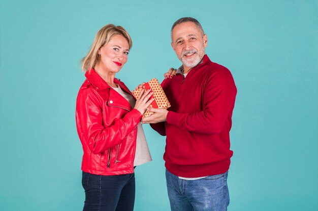 Retrato de hombre maduro sonriente dando presente a su esposa en chaqueta roja