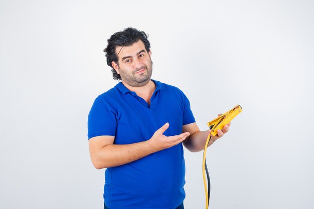 Retrato de hombre maduro, sosteniendo herramientas de construcción en camiseta azul y mirando pensativo vista frontal