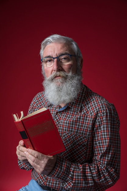Retrato de un hombre mayor con barba gris mirando a la cámara contra el telón de fondo rojo
