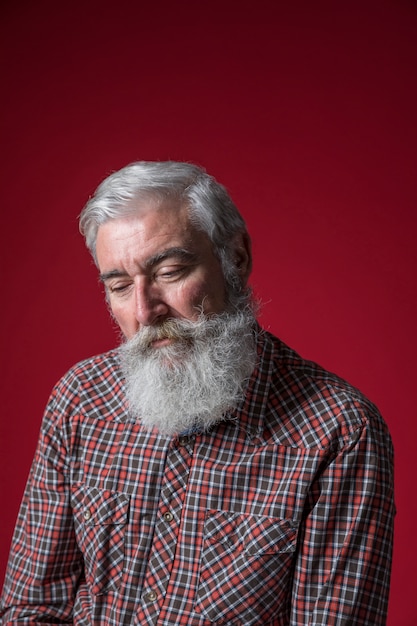 Retrato de un hombre mayor deprimido contra fondo rojo