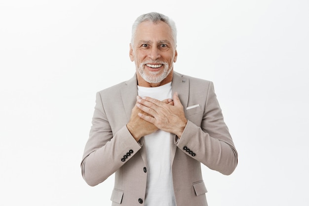 Retrato de hombre mayor emocionado feliz mirando halagado y asombrado, tomados de la mano sobre el pecho