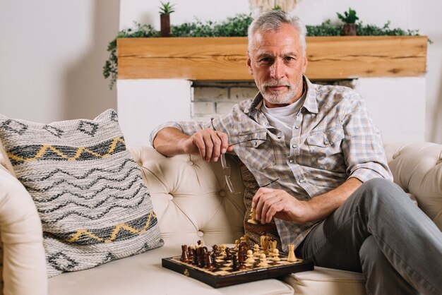 Retrato de un hombre mayor sentado en el sofá jugando al ajedrez