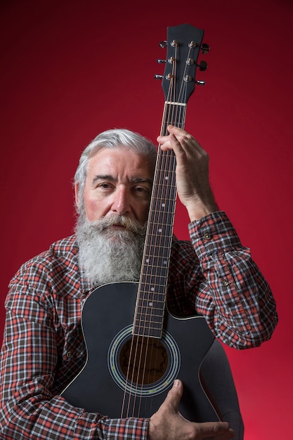 Retrato de un hombre mayor serio con la guitarra en su mano contra el fondo rojo