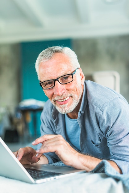 Retrato del hombre mayor sonriente que usa la computadora portátil