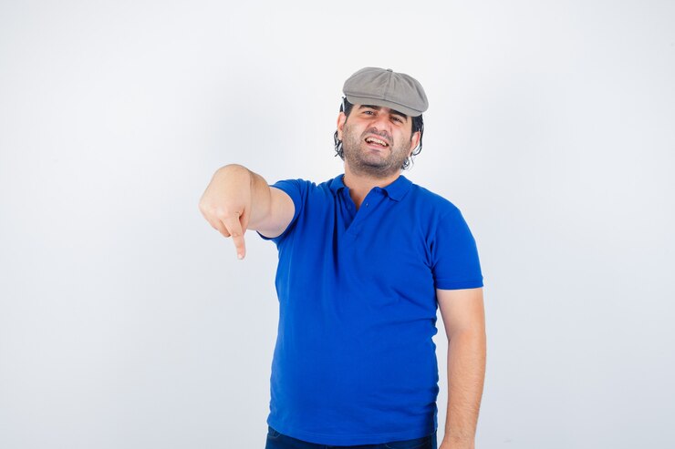 Foto gratuito retrato de hombre de mediana edad apuntando hacia abajo en la camiseta de polo, sombrero de hiedra y mirando molesto vista frontal