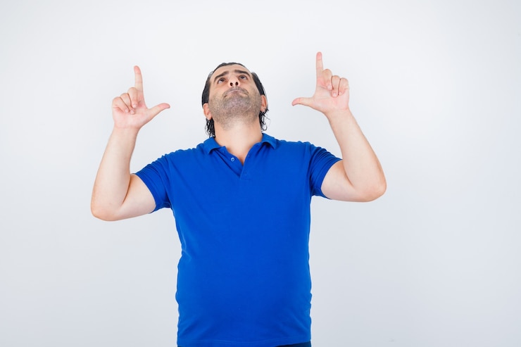 Foto gratuito retrato de hombre de mediana edad apuntando hacia arriba en camiseta azul y mirando confiado
