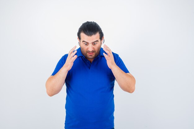 Foto gratuita retrato de hombre de mediana edad levantando las manos sobre el pecho en camiseta azul y mirando perplejo