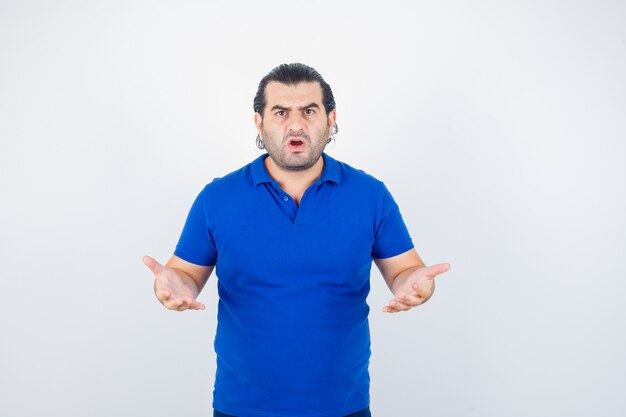 Retrato de hombre de mediana edad manteniendo las manos de manera agresiva en camiseta azul y de aspecto estresado