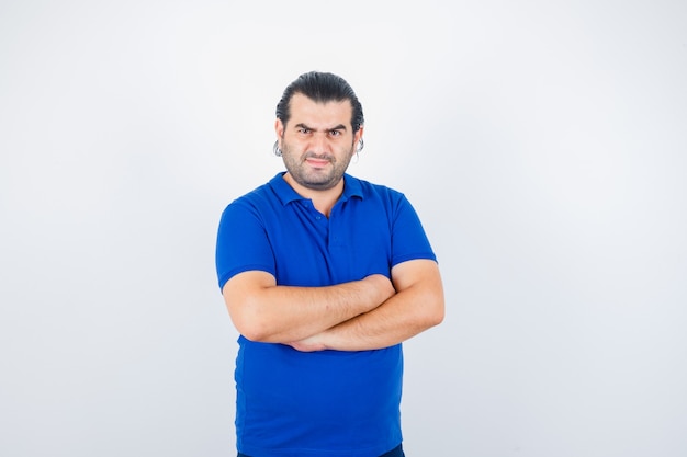 Retrato de hombre de mediana edad de pie con los brazos cruzados en camiseta azul y mirando confiado