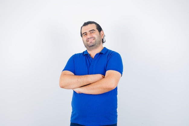 Retrato de hombre de mediana edad de pie con los brazos cruzados en camiseta azul y mirando feliz