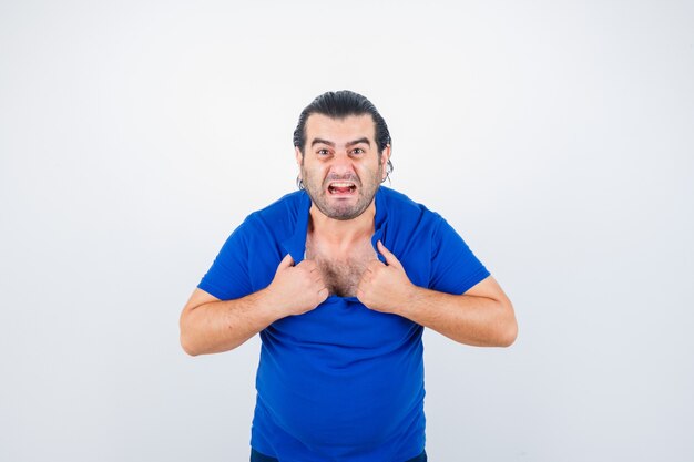 Retrato de hombre de mediana edad rasgando su camiseta con actitud furiosa