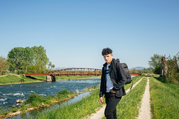 Retrato de hombre con mochila de pie cerca del río