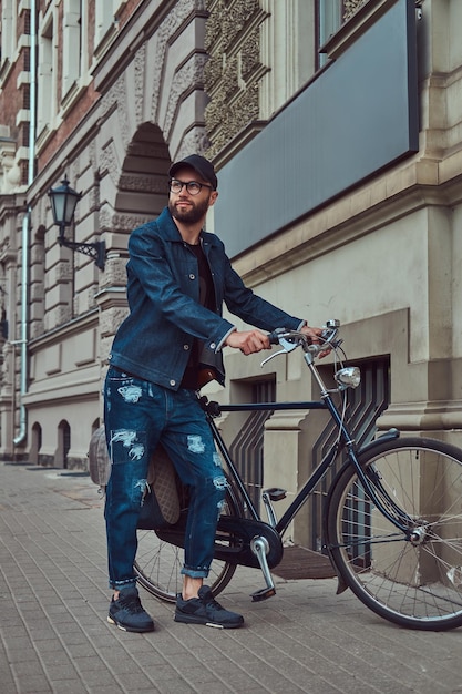 Retrato de un hombre de moda con ropa elegante caminando con bicicleta de ciudad en la calle.