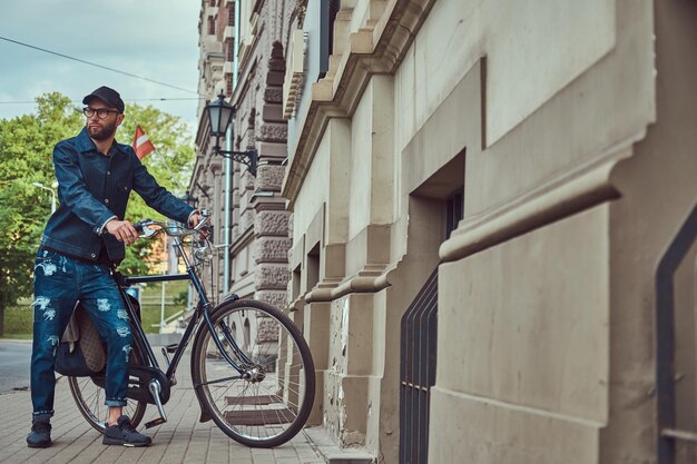 Retrato de un hombre de moda con ropa elegante caminando con bicicleta de ciudad en la calle.