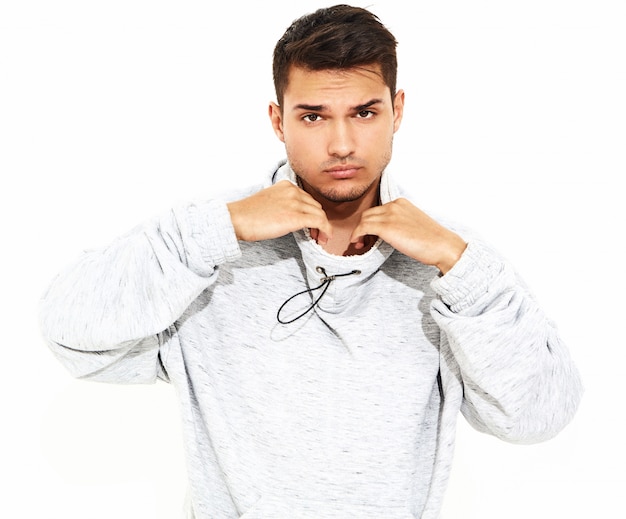 El retrato del hombre modelo hermoso joven se vistió en la ropa con capucha casual gris que presentaba en la pared blanca. aislado