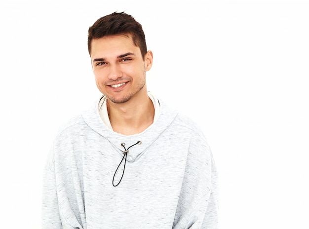 Foto gratuita el retrato del hombre modelo hermoso sonriente de los jóvenes se vistió en la ropa con capucha casual gris que presentaba en la pared blanca. aislado