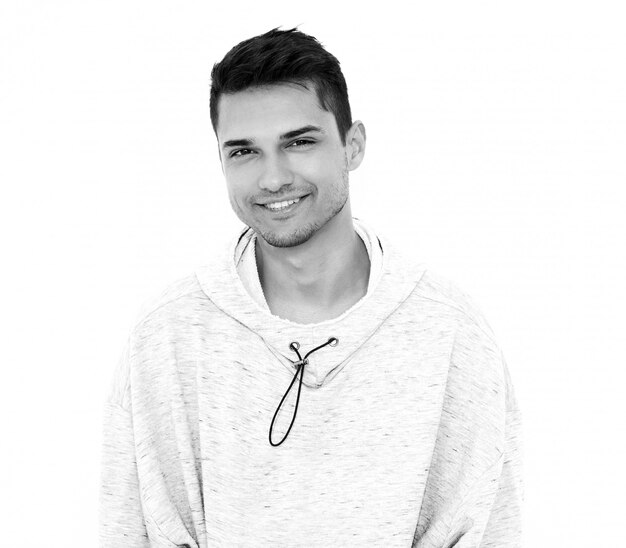 El retrato del hombre modelo hermoso sonriente de los jóvenes se vistió en la ropa con capucha casual gris que presentaba en la pared blanca. Aislado