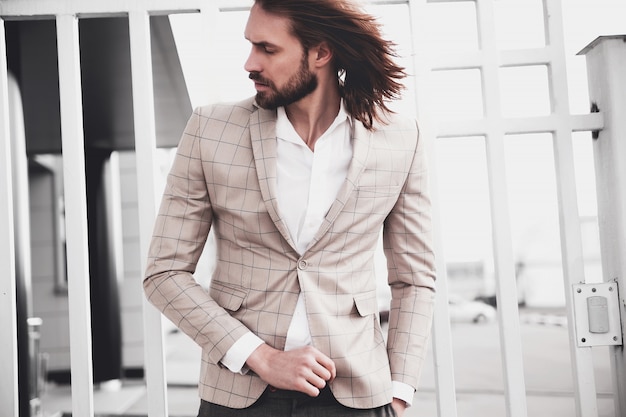 Retrato de hombre de modelo masculino de moda guapo sexy vestido con elegante traje a cuadros beige posando en el fondo de la calle