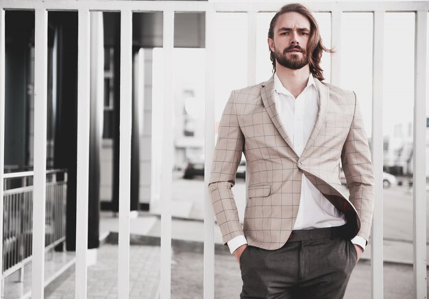 Retrato de hombre de modelo masculino de moda guapo sexy vestido con elegante traje a cuadros beige posando en el fondo de la calle