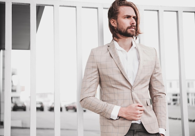 Retrato de hombre de modelo masculino de moda guapo sexy vestido con elegante traje a cuadros beige posando en el fondo de la calle