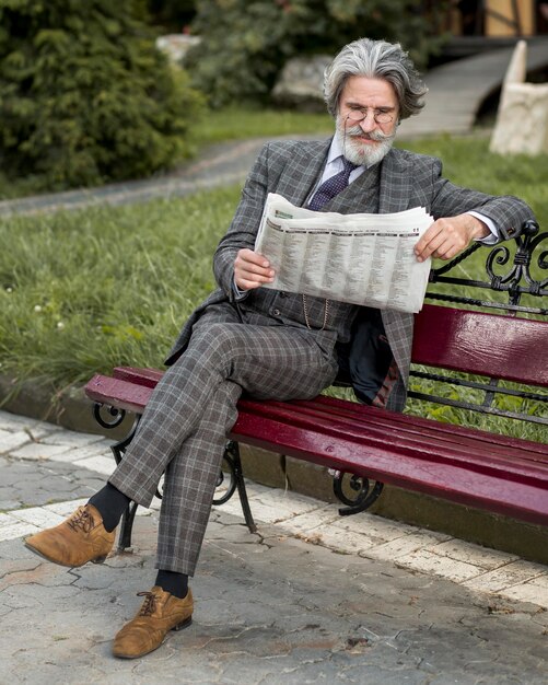 Retrato de hombre moderno leyendo el periódico en un banco