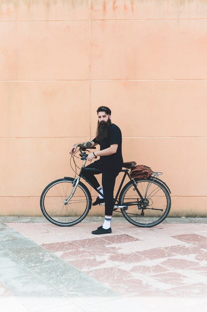 Retrato de un hombre moderno de pie con su bicicleta contra la pared