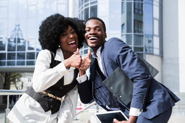 Foto gratuita retrato de un hombre y de una mujer africanos felices jovenes que muestran los pulgares para arriba