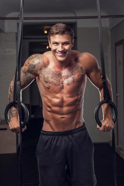 Retrato de un hombre musculoso entrenando con anillos en un gimnasio.