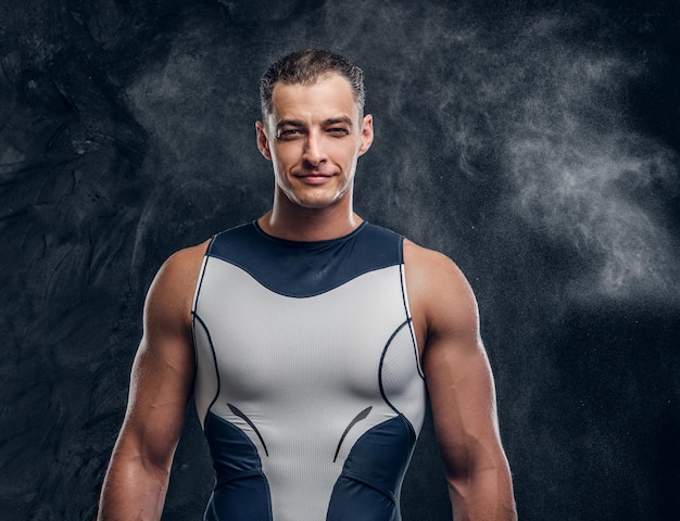 Foto gratuita retrato de un hombre musculoso y guapo con traje de neopreno y con una nube de talco alrededor sobre un fondo oscuro.