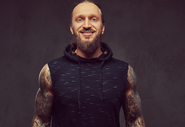 Retrato de un hombre musculoso tatuado con barba y un elegante corte de pelo con ropa deportiva negra. aislado en un fondo oscuro.