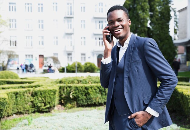 Retrato de un hombre de negocios africano joven sonriente que habla en el teléfono móvil