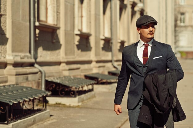 Retrato de un hombre de negocios árabe inglés retro de la década de 1920 con traje oscuro, corbata y gorra plana caminando por calles antiguas