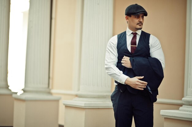 Retrato de un hombre de negocios árabe inglés retro de la década de 1920 con traje oscuro, corbata y gorra plana