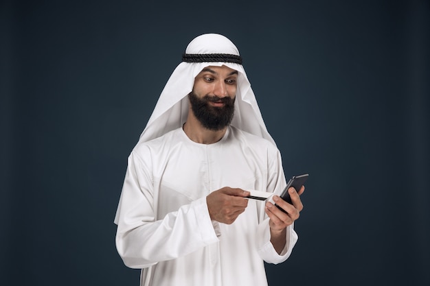 Retrato de hombre de negocios de Arabia Saudita. Hombre con smartphone para pagar facturas, compras en línea o apuestas. Concepto de negocio, finanzas, expresión facial, emociones humanas.
