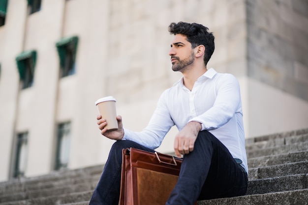 Retrato de un hombre de negocios bebiendo una taza de café en un descanso del trabajo mientras está sentado en las escaleras al aire libre. Concepto de negocio.