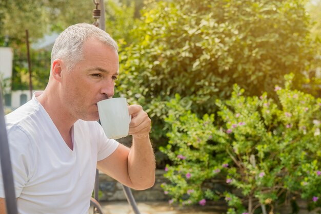 Retrato de un hombre de negocios confidente que se sienta en el banco y que bebe el café al aire libre. Hombre de negocios bebiendo café en el jardín. Tono vintage.