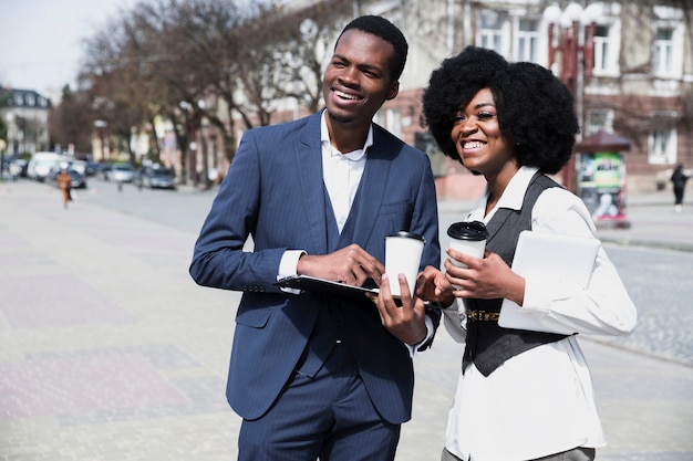 Retrato de un hombre de negocios y de una empresaria jovenes africanos que sostienen la taza de café disponible en la ciudad