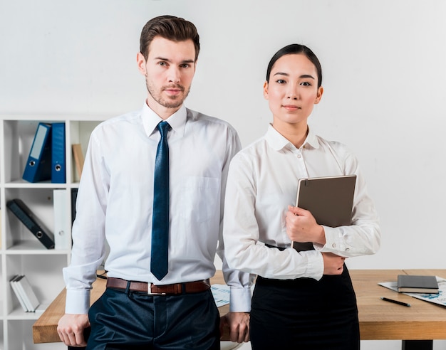 Retrato del hombre de negocios y de la empresaria jovenes confiados que se colocan delante del escritorio