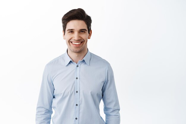 Retrato de hombre de negocios exitoso, ceo trabajador de oficina feliz sonriendo complacido, de pie contra el fondo blanco en camisa de cuello azul