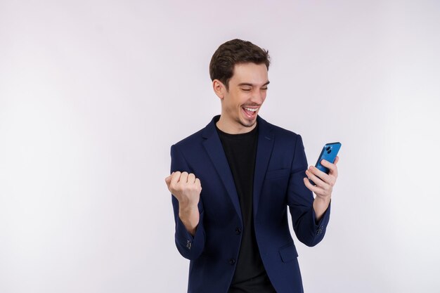 Retrato de un hombre de negocios feliz que usa un teléfono inteligente y hace un gesto de ganador apretando el puño sobre fondo blanco