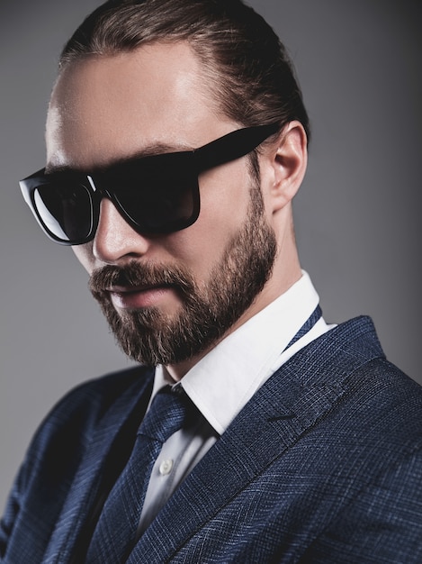 Retrato de hombre de negocios guapo modelo vestido con elegante traje azul con gafas de sol