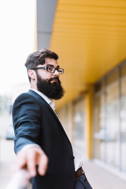 Retrato del hombre de negocios joven de la barba con las lentes negras que miran lejos